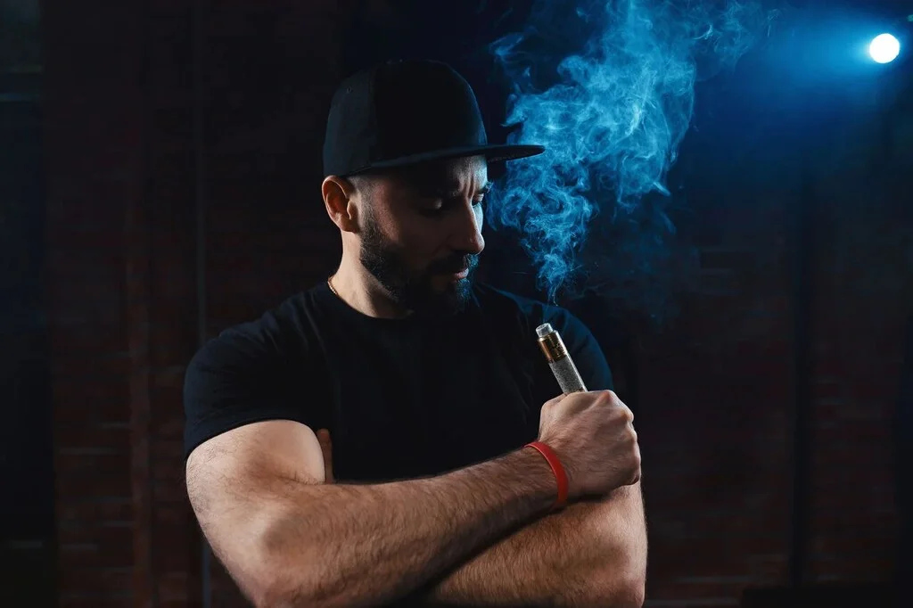 Homem vaporizando com um pod recarregável, mostrando a experiência de vape após adicionar essência ao dispositivo, de acordo com o processo de como colocar essência no pod recarregável.